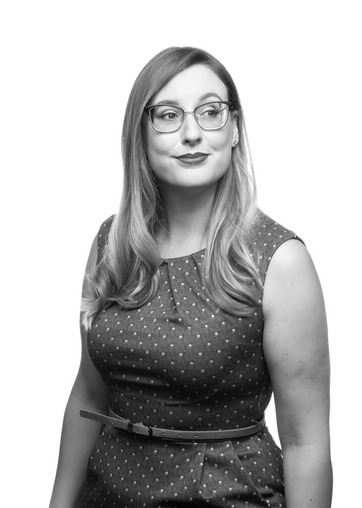 Jill Scheyk, wine tasting event leader, looks off to the side with one raised eyebrow and a cheeky smirk. She has librarian glasses and a polka dot dress.